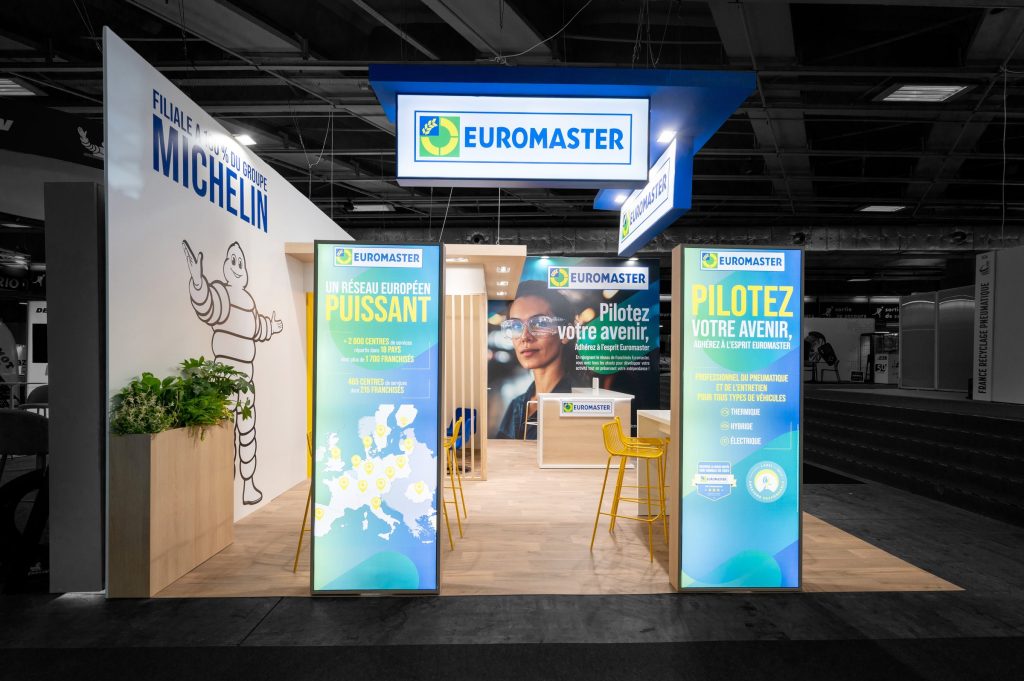 Vue de côté du stand sur-mesure de 33 m² réalisé par R2 Stand pour Euromaster sur le salon Equipauto avec le comptoir d'accueil et le partenariat avec Michelin