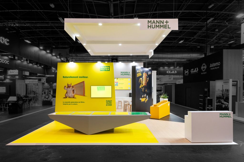 Vue de face du stand sur-mesure réalisé par l'agence R2 Stand Lyon sur le salon Equipauto pour son client Mann+Hummel avec son imposant comptoir de présentation et sa haute enseigne