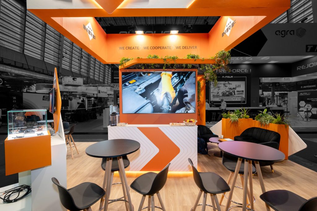 Vue de l'intérieur du stand sur-mesure aux couleurs orange et blanc réalisé par R2 Stand pour NRF sur le salon Equipauto ses différents espaces réceptifs, le bar, le salon et les tables hautes