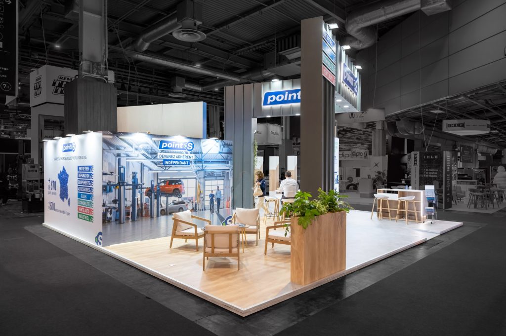 Photo de l'angle arrière du stand sur-mesure réalisé par l'agence R2 Stand Lyon pour son client Point S mettant en avant les différentes zones de réception ainsi que la signalétique et l'enseigne imposante du stand