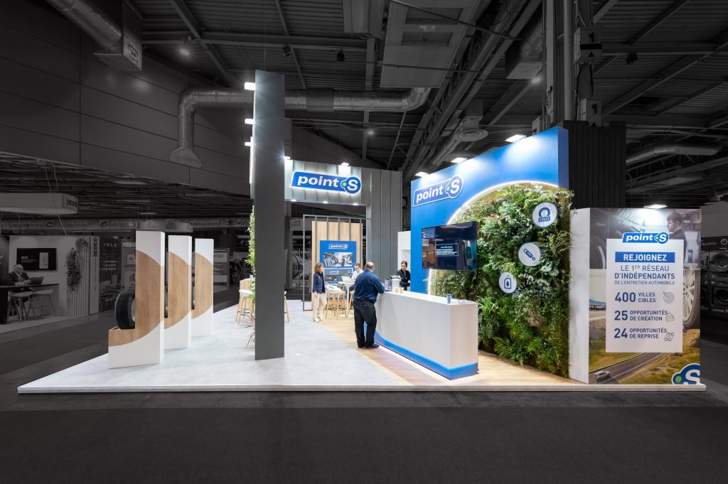 Photo du côté du stand sur-mesure réalisé par l'agence R2 Stand Lyon pour son client Point S et de son comptoir d'accueil ainsi que son mur végétalisé