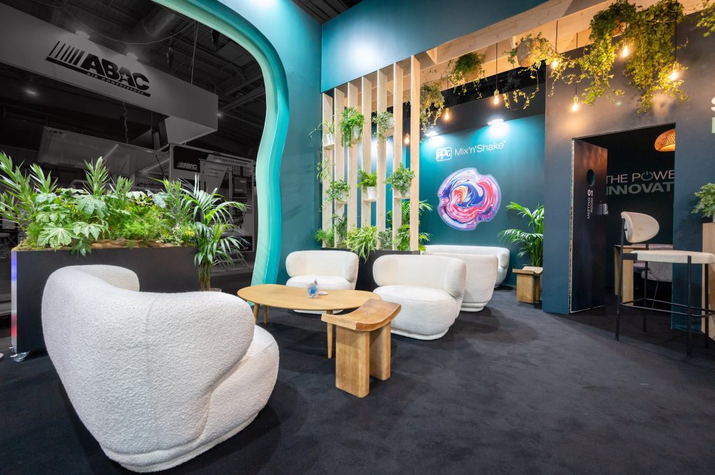 Photo des salons d'accueil réalisé par R2 Stand pour PPG sur Equipauto sous les arches colorées du stand sur-mesure et séparé par une cloison végétalisée