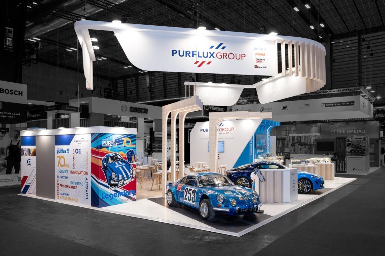 Photo d'angle du stand sur-mesure réalisé par R2 Stand pour Purflux sur Equipauto mettant la signalétique qui habille l'espace bar et réception du stand ainsi que les deux voitures mise en avant sous des arches lumineuses