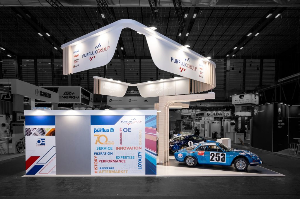 Photo d'un côté du stant sur-mesure réalisé par R2 Stand pour Purflux sur Equipauto mettant la signalétique qui habille l'espace bar et réception du stand ainsi que l'Alpine de collection mise en avant par les arches lumineuses
