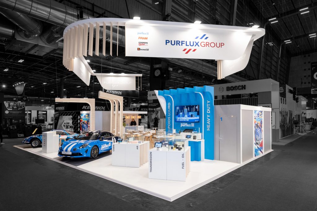 Photo depuis l'angle d'attaque du stand sur-mesure Purflux réalisé par R2 Stand sur Equipauto mettant en avant les podiums de présentation des produits pour la gamme poids lourds ainsi que les voitures customisées