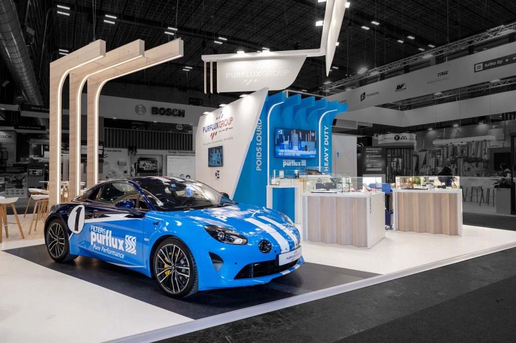 Photo du stand sur mesure Purflux réalisé par R2 Stand sur Equipauto mettant en avant une Alpine customisée aux couleurs de la marque ainsi que les podiums de présentation des produits sous vitrine