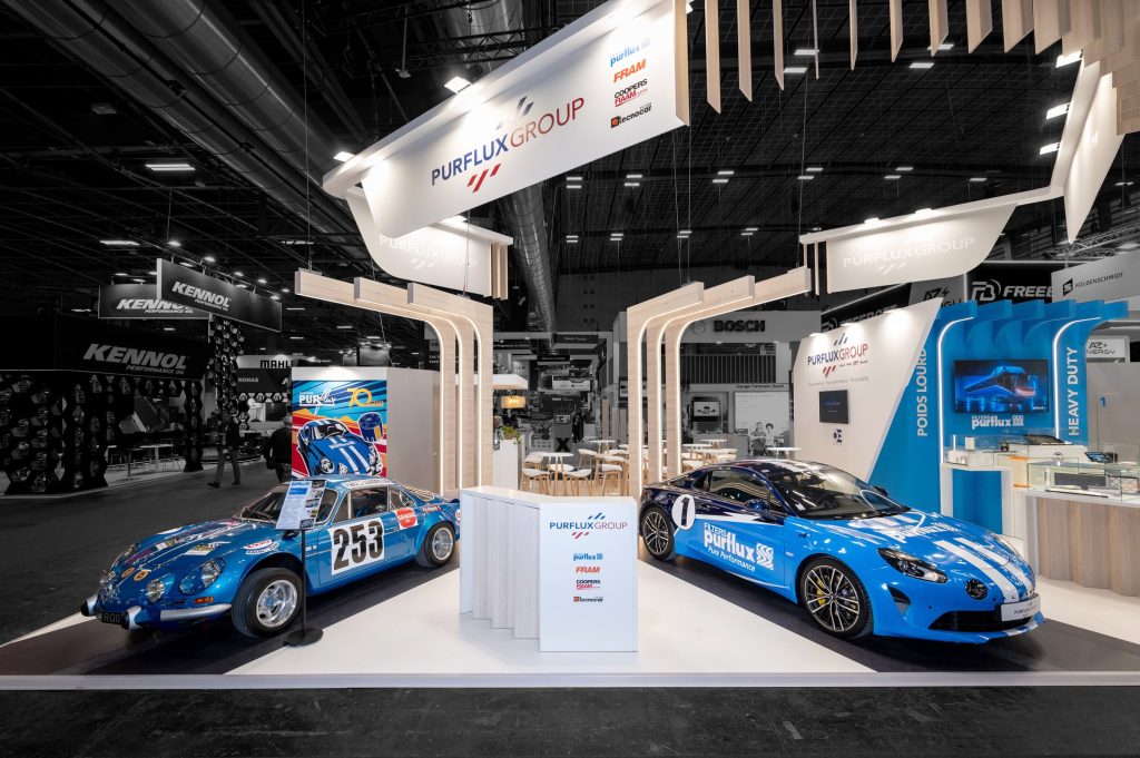 Photo of the custom-made Purflux stand created by R2 Stand at Equipauto, showcasing two Alpines customized in the brand's colors to celebrate the group's 70th anniversary. The cars are highlighted by custom-made light arches and the imposing high sign.